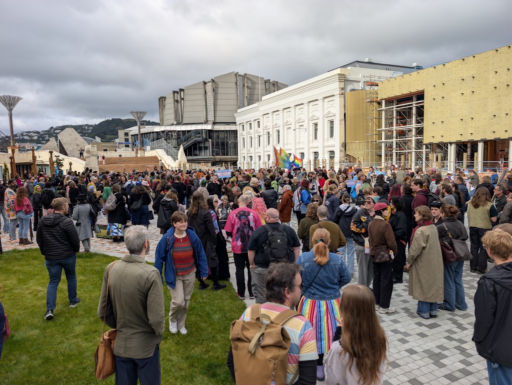 A large crowd of people gathered in a plaza near several buildings.
