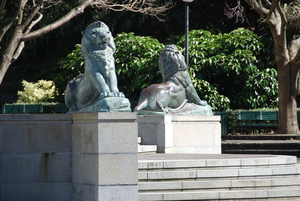 Two bronze lion statues on pedestals in a park set