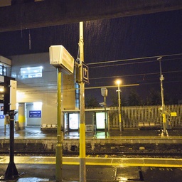 A train station platform at night under the rain.