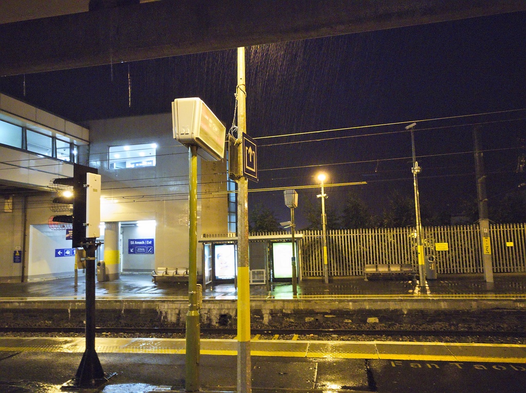 A train station platform at night under the rain.