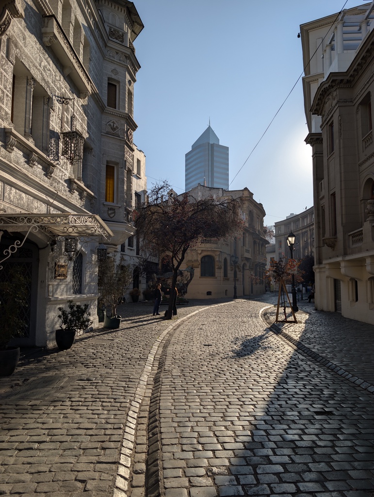 A cobblestone street in a city with tall buildings and a skyscraper in the background.