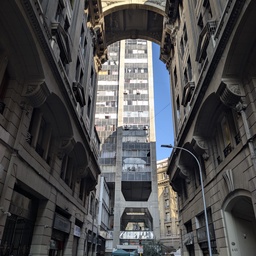 Tall, narrow street flanked by classic architecture and an overhead bridge.