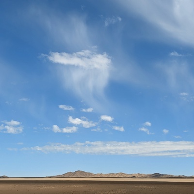 A vast desert landscape under a blue sky with wispy clouds.
