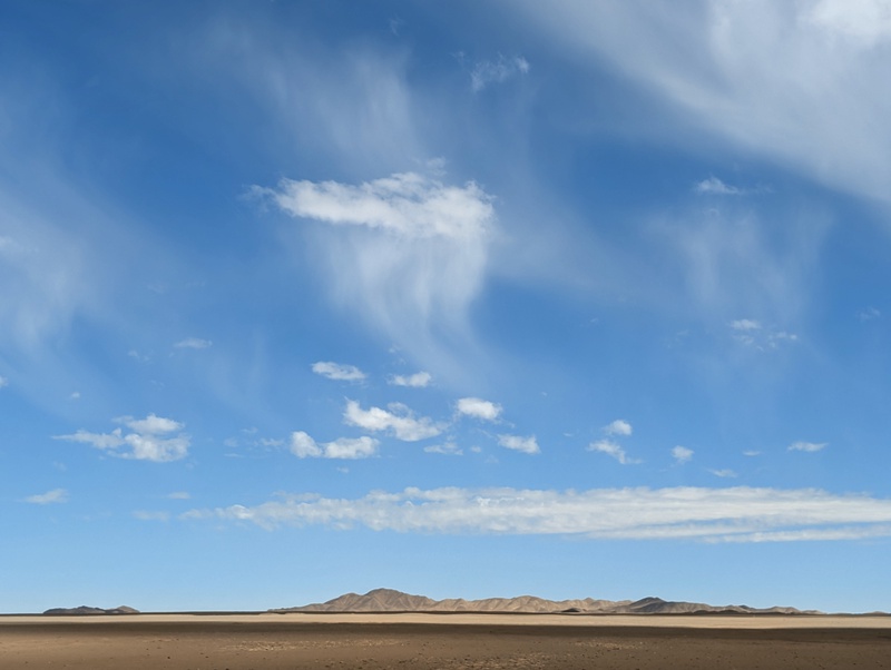 A vast desert landscape under a blue sky with wispy clouds.
