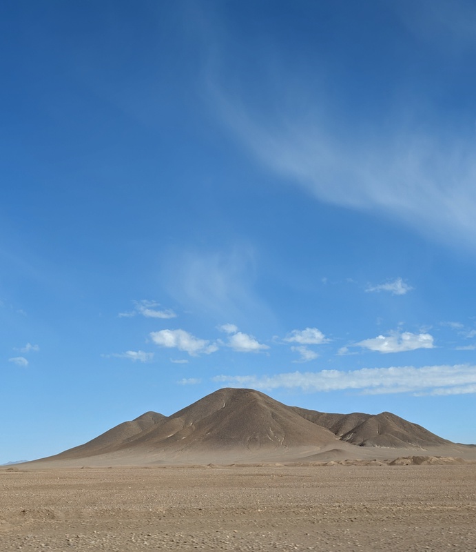 A lone desert mountain under a bright blue sky.