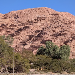 A large, reddish-brown mountain with ancient ruins on its slope.