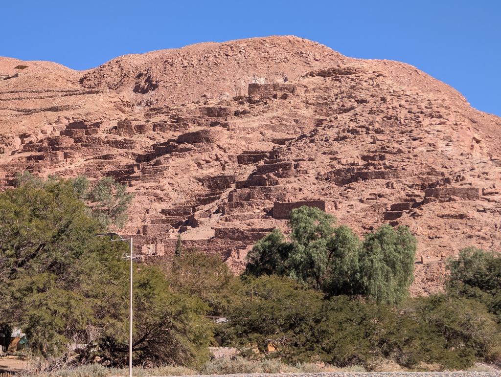 A large, reddish-brown mountain with ancient ruins on its slope.