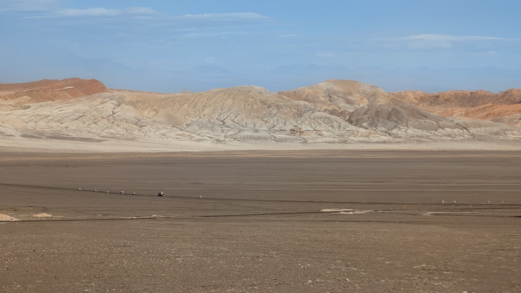 A vast, barren landscape of pale hills and a flat desert plain.